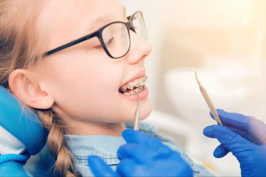 A young girl with glasses receiving an orthodontic adjustment for her silver braces at a dental clinic