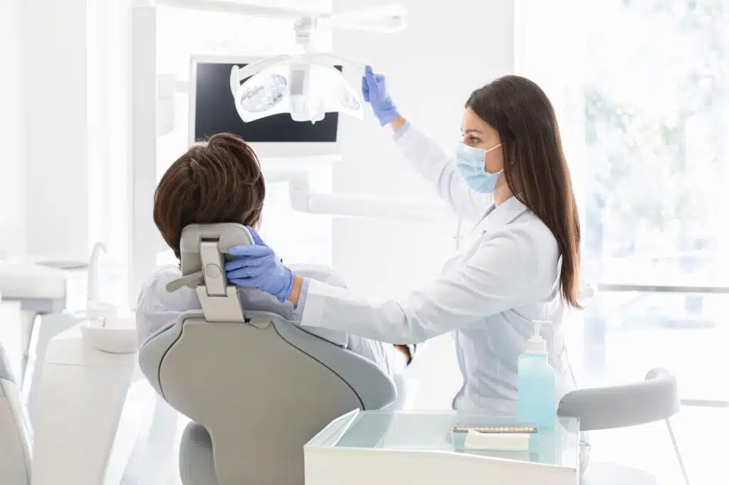 A female dentist adjusting the overhead exam light over a patient.
