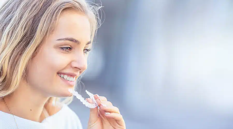 Smiling young woman holding a clear Invisalign orthodontic aligner